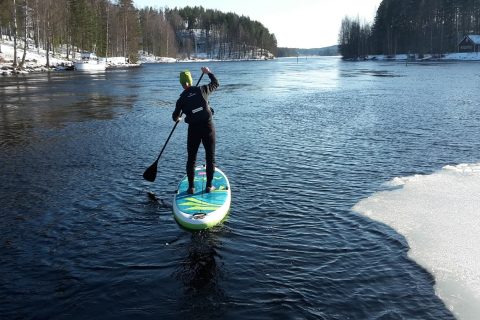 Henkilö sup-laudalla talvisessa maisemassa